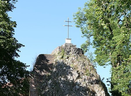 Ein hoher Felsblock trägt ein Kreuz obenauf und eine Inschrifttafel.