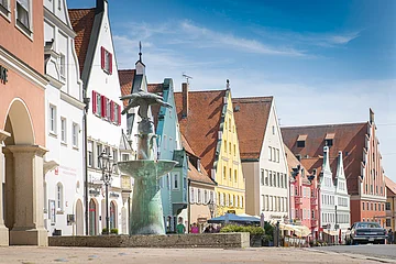 Reichsstraße Donauwörth Straße mit bunten Giebelhäusern und einem Brunnen im Vordergrund. Klarer Himmel im Hintergrund.