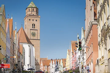 Straßenszene mit bunten Gebäuden und einem Kirchturm im Hintergrund, Ampel im Vordergrund.