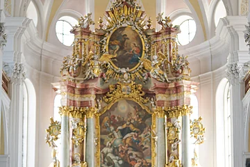 Zwei Personen mit Rucksäcken stehen in einer Kirche vor einem reich verzierten Altar.