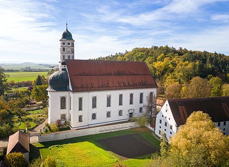 Wallfahrtskirche Maihingen Eine große Kirche aus der Luft. Darum herum andere Gebäude, grüne Wiese und ein Hügel mit grünen Bäumen.