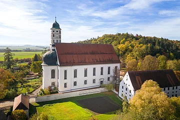 Eine große Kirche aus der Luft. Darum herum andere Gebäude, grüne Wiese und ein Hügel mit grünen Bäumen.